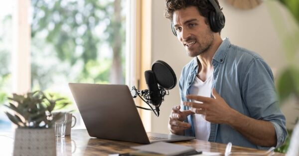Junger Mann am Laptop spricht in ein Mikrophon