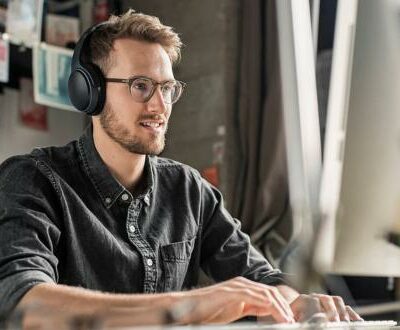 Junger Mann sitzt mit Kopfhörern aufmerksam vor dem Bildschirm in unserem Online Marketing Manager Kurs