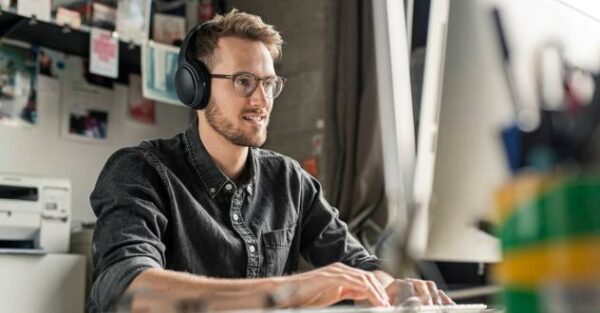 Junger Mann sitzt mit Kopfhörern aufmerksam vor dem Bildschirm in unserem Online Marketing Manager Kurs