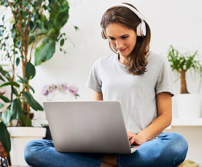 Eine junge Frau sitzt im Schneidersitz vor ihrem aufgeklappten Laptop mit Kopfhörern