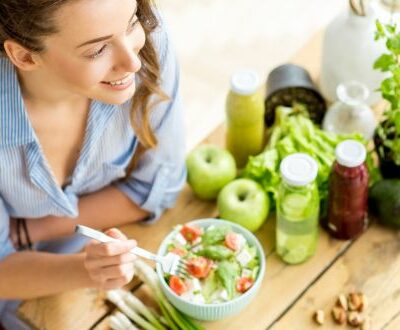 Eine Frau sitzt am Esstisch vor einer Schüssel Salat, Gemüse und Kräutern in unserem Ernährungscoaching