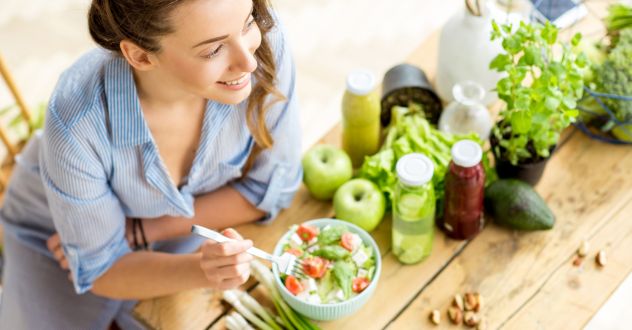 Eine Frau sitzt am Esstisch vor einer Schüssel Salat, Gemüse und Kräutern in unserem Ernährungscoaching