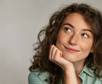 Eine Frau hat ihr Gesicht in die Handfläche gestützt und schaut lächelnd nach oben in unserem Female Health Coaching