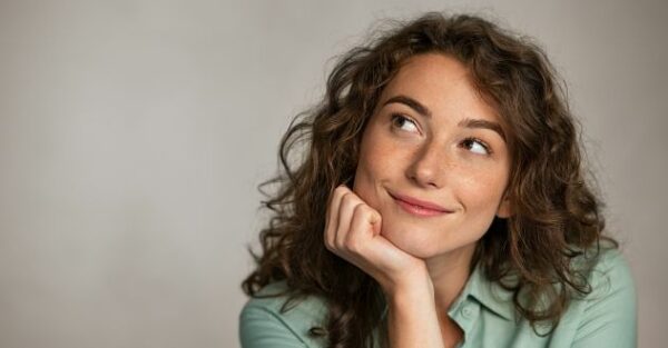 Eine Frau hat ihr Gesicht in die Handfläche gestützt und schaut lächelnd nach oben in unserem Female Health Coaching