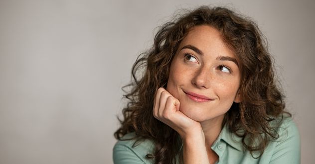 Eine Frau hat ihr Gesicht in die Handfläche gestützt und schaut lächelnd nach oben in unserem Female Health Coaching