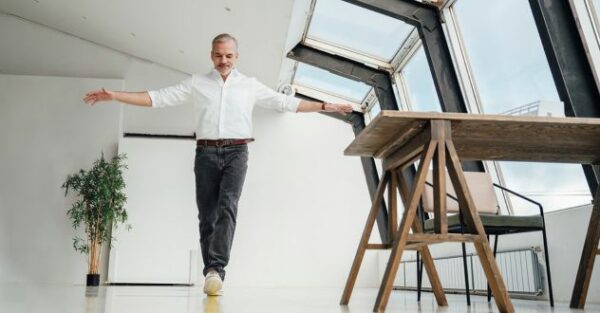 Ein Mann balanciert auf einer imaginären Linie mit ausgebreiteten Händen durch ein helles Arbeitszimmer
