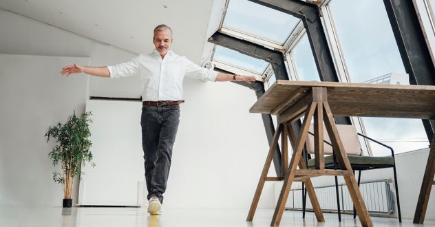 Ein Mann balanciert auf einer imaginären Linie mit ausgebreiteten Händen durch ein helles Arbeitszimmer