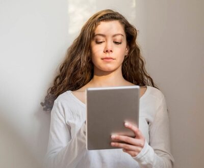 Eine junge Frau steht mit dem Rücken an einer Wand und schaut auf ein Tablet in ihrer Hand in unserem Karrierecoaching für Berufseinsteiger:innen