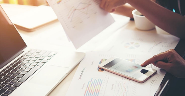 Schreibtisch mit Laptop, Taschenrechner und Kalkulationspapiere in unserem Businessplan Coaching