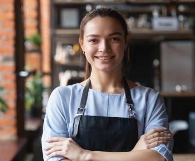 Eine Frau steht mit verschränkten Armen zufrieden in einer Küche und lächelt in unserem Gastronomie Coaching