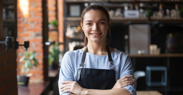Eine Frau steht mit verschränkten Armen zufrieden in einer Küche und lächelt in unserem Gastronomie Coaching