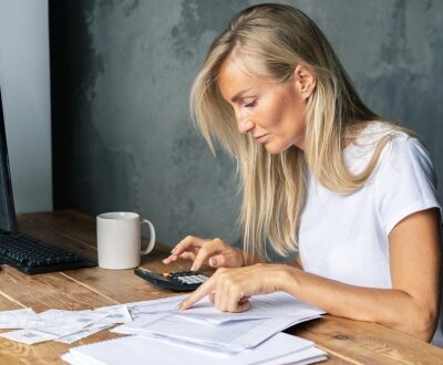 Frau itzt am Schreibtisch und kalkuliert mit einem Taschenrechner in unserem Finanzcoaching
