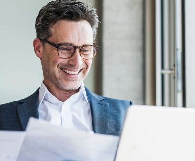 Ein Mann sitzt vor einem Laptop und schaut sich Unterlagen an in unserem Führungskräftecoaching.