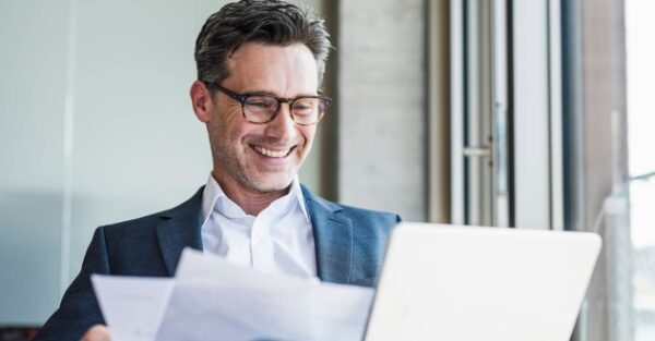 Ein Mann sitzt vor einem Laptop und schaut sich Unterlagen an in unserem Führungskräftecoaching.
