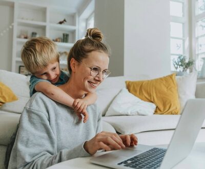 Eine Mutte mit Kind sitzt vor dem Sofa am Laptop in unserem Karrierecoaching für Mütter