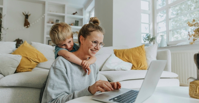 Eine Mutte mit Kind sitzt vor dem Sofa am Laptop in unserem Karrierecoaching für Mütter