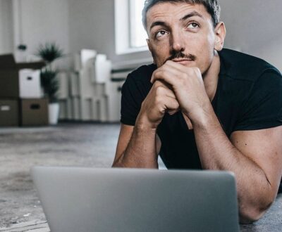Ein Mann liegt mit aufgeklapptem Laptop auf dem Boden und schaut nachdenklich nach oben in unserem Orientierungscoaching.