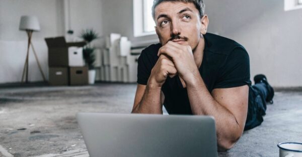 Ein Mann liegt mit aufgeklapptem Laptop auf dem Boden und schaut nachdenklich nach oben in unserem Orientierungscoaching.