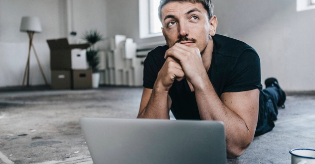 Ein Mann liegt mit aufgeklapptem Laptop auf dem Boden und schaut nachdenklich nach oben in unserem Orientierungscoaching.