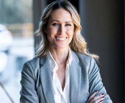 Eine Frau im Businessoutfit lächelt mit verschränkten Armen in die Kamera in unserem Vertriebscoaching