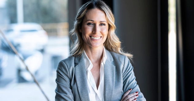 Eine Frau im Businessoutfit lächelt mit verschränkten Armen in die Kamera in unserem Vertriebscoaching