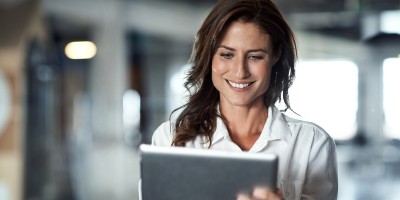 Junge Frau schaut lächelnd auf ihr Tablet