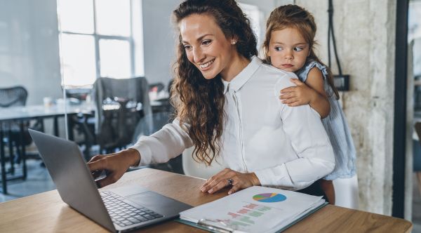 Ein Mutter sitzt am Laptop, das Kind steht hinter ihr und schaut zu