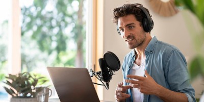 Junger Mann spricht mit Kopfhörern am Laptop in ein Tischmikro in unserer Content Marketing Manager Weiterbildung