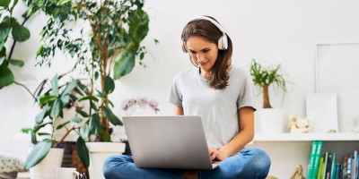 Junge Frau sitzt mit Kopfhörern und Laptop im Schneidersitz auf dem Boden in unserer Online Marketing Weiterbildung