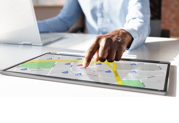 Mann sitzt am Laptop und zeit auf eine digitale Map am Tablet