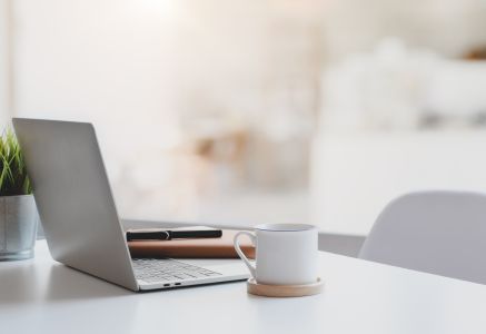 Schreibtischansicht mit aufgeklapptem Laptop Kaffeetasse, Organizer und Pflanze