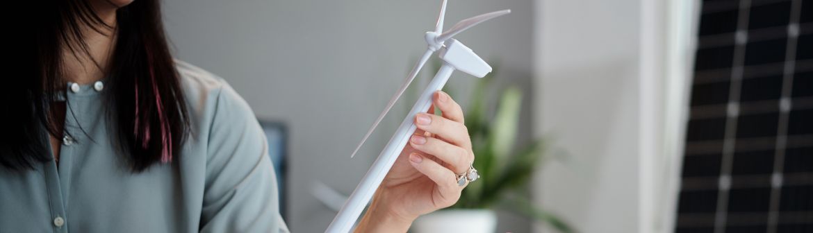 Trendberufe: Eine Frau in einem modernen Büro hält ein kleines Windrad-Modell in der Hand, während im Hintergrund eine Solarpanel-Wand zu sehen ist – ein Symbol für nachhaltige Zukunftsberufe