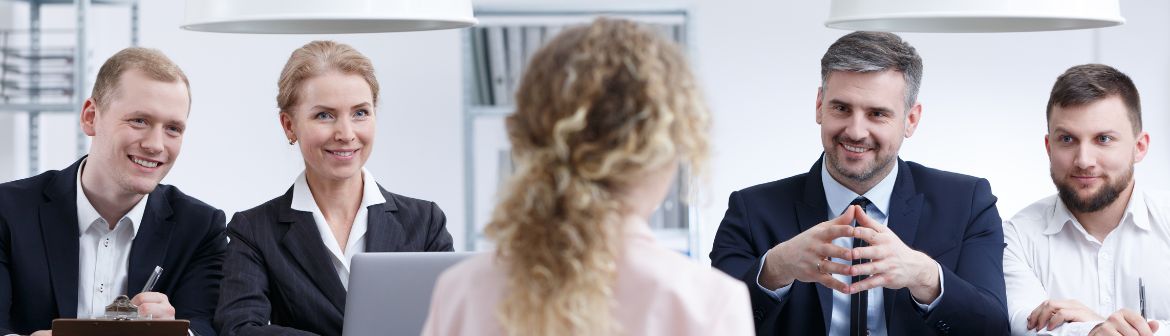 Eine Bewerberin sitzt vor einem lächelnden vierköpfigen Interview-Team in einem modernen Büro. Die Gesprächspartner wirken professionell und stellen Fragen im Bewerbungsgespräch