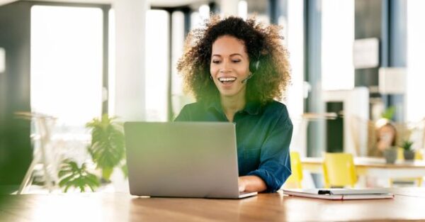 Eine lächelnde Frau mit Headset arbeitet als KI Managerin an ihrem Laptop in einem modernen Büro.