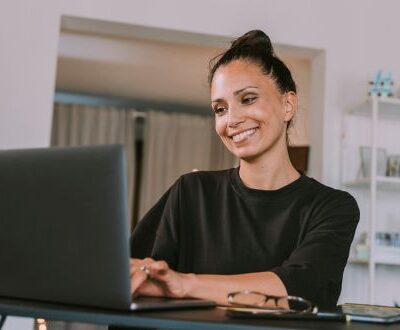 Eine lächelnde Frau arbeitet an ihrem Laptop in einem modernen Homeoffice und setzt agile Arbeitsmethoden ein.