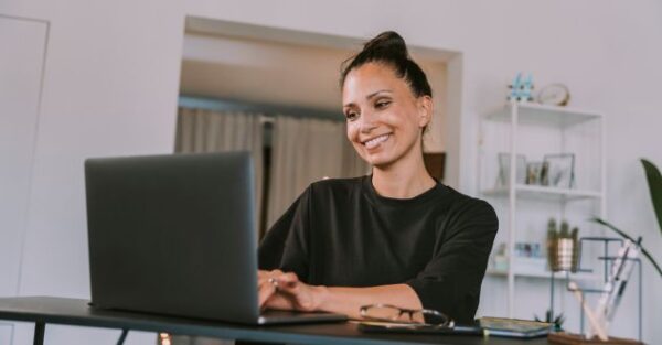 Eine lächelnde Frau arbeitet an ihrem Laptop in einem modernen Homeoffice und setzt agile Arbeitsmethoden ein.