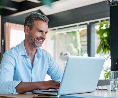 Ein lächelnder Mann arbeitet an seinem Laptop in einer modernen, lichtdurchfluteten Umgebung und nutzt eine KI-Anwendung
