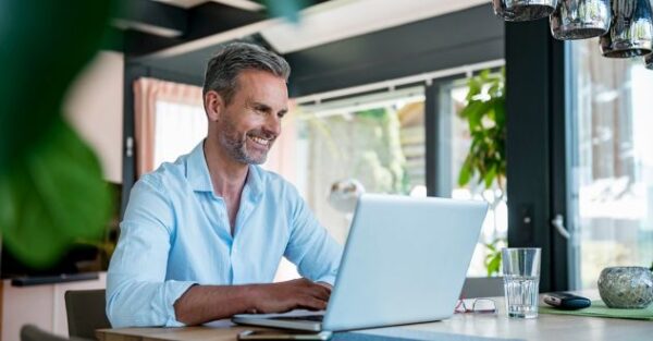 Ein lächelnder Mann arbeitet an seinem Laptop in einer modernen, lichtdurchfluteten Umgebung und nutzt eine KI-Anwendung