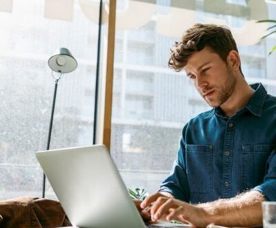 Ein junger Mann arbeitet konzentriert an seinem Laptop in einem modernen, lichtdurchfluteten Café. Er beschäftigt sich mit einer strategischen KI-Implementierung im Rahmen einer Weiterbildung. Das Bild vermittelt digitales Lernen, Selbststudium und den professionellen Einsatz von Künstlicher Intelligenz für innovative Geschäftsstrategien